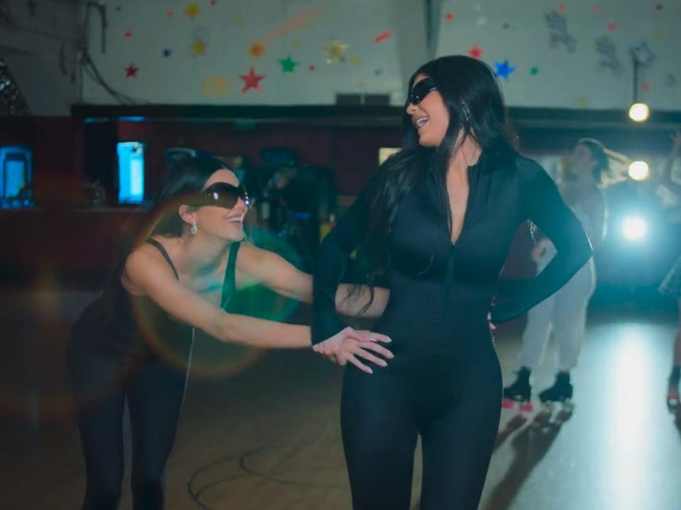 kendall and kylie jenner roller skating. they're both wearing black shapewear and sunglasses, and kendall is holding onto kylie's waist. they're both smiling widely and looking at each other