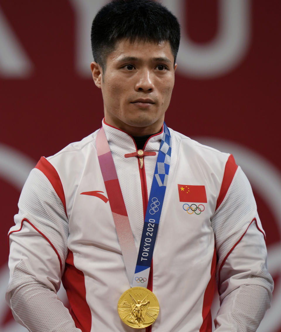 Li Fabin of China celebrates on the podium after winning the gold medal and setting an Olympic record in the men's 61kg weightlifting event, at the 2020 Summer Olympics, Sunday, July 25, 2021, in Tokyo, Japan. (AP Photo/Luca Bruno)