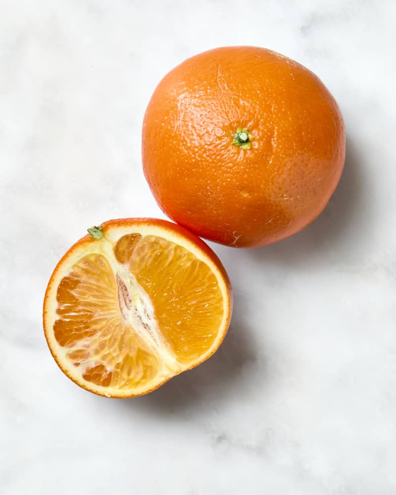 overhead shot of one whole and one half tangerine  on a white marble surface.