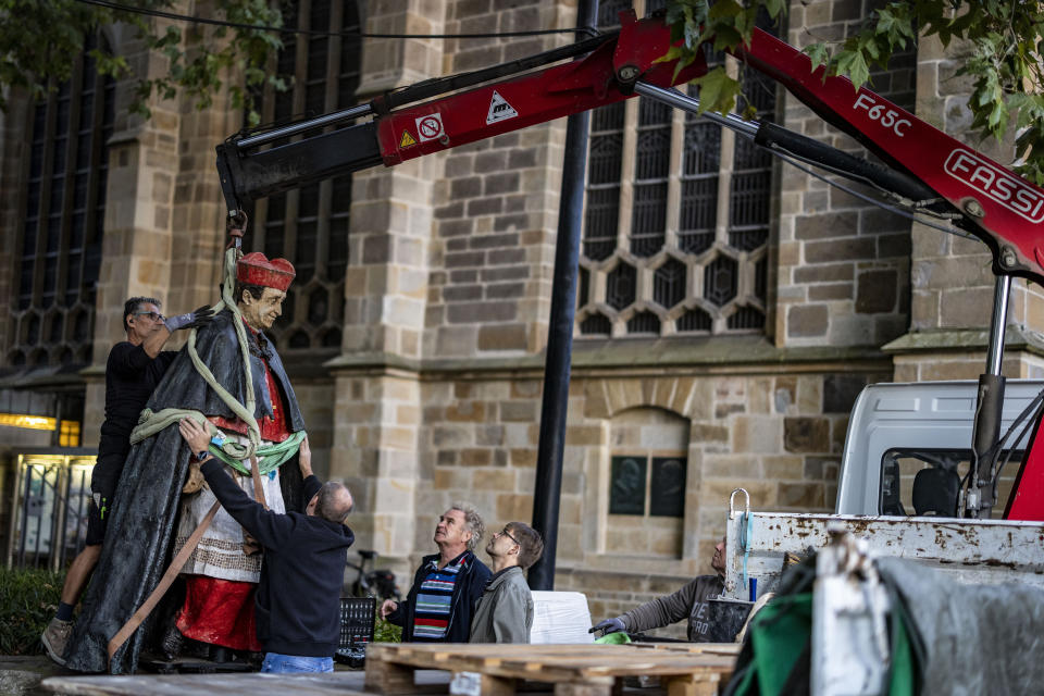 The sculpture of Essen Cardinal Franz Hengsbach hangs on a crane in front of Essen Cathedral after being dismantled and loaded onto a truck in Essen, Germany, Monday Sept. 25, 2023. A statue of a deceased German cardinal was removed from its perch outside Essen Cathedral in western Germany on Monday, days after allegations of sexual abuse decades ago became public. (Christoph Reichwein/dpa via AP)