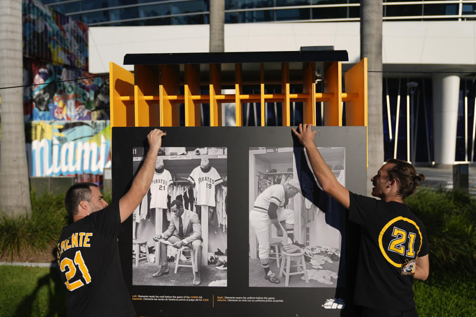 Exhibit designer Luisel Zayas, left, and a colleague wear shirts with late Major League Baseball player Roberto Clemente's number 21 as they install a traveling exhibit titled "3000" in a nod to his 3000 career hits, at Miami Marlins' loanDepot Park in Miami, Wednesday, Jan. 31, 2024. The tribute to the Pittsburgh Pirates outfielder will be on display at the park during baseball's Caribbean Series, which runs from Feb. 1 through Feb. 9. (AP Photo/Rebecca Blackwell)
