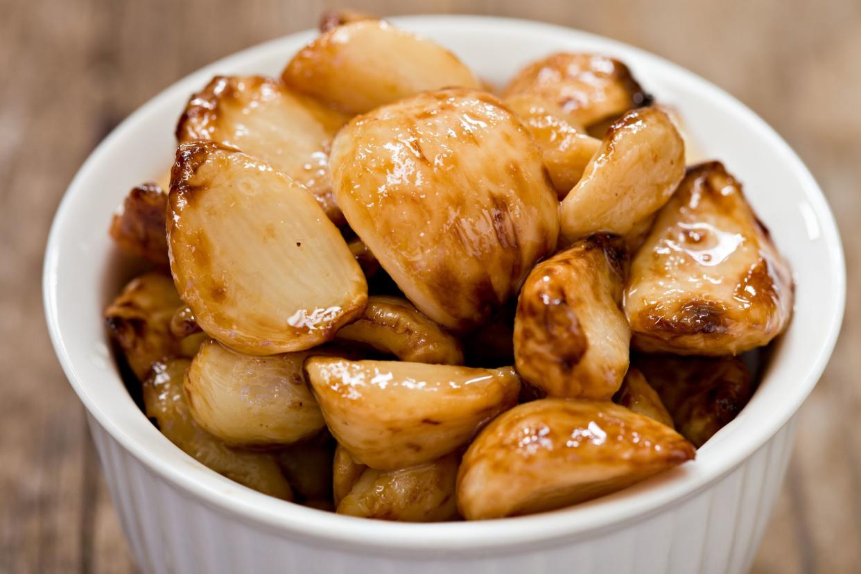 A high angle extreme close up of a small white bowl full of roasted garlic cloves.