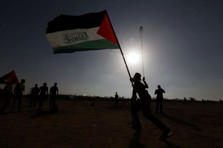 Demonstrator holding a Palestinian flag uses a sling to hurl stones at Israeli forces during a protest at the Israel-Gaza border fence, in the southern Gaza Strip