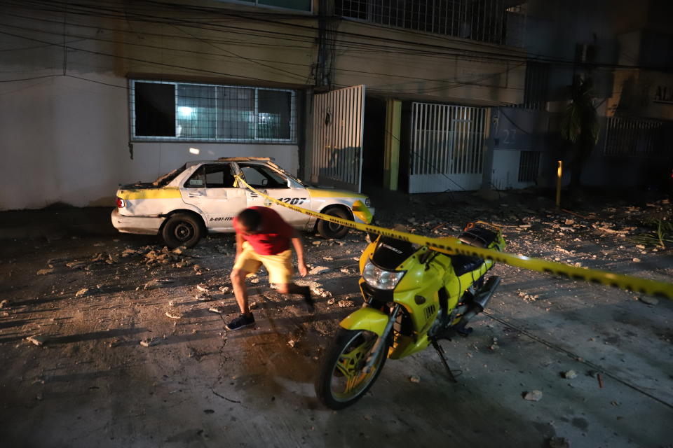 A man ducks under police tape, on a street covered with debris after a strong earthquake in Acapulco, Mexico, Tuesday, Sept. 7, 2021. The quake struck southern Mexico near the resort of Acapulco, causing buildings to rock and sway in Mexico City nearly 200 miles away. (AP Photo/ Bernardino Hernandez)