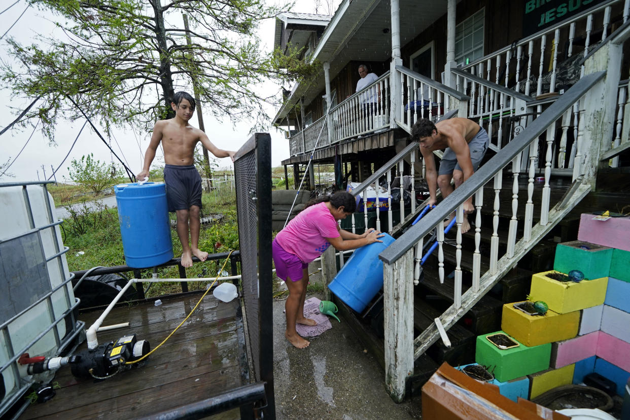 Lerryn Brune, 10, center, Terren Dardar, 17, right, and Dayton Verdin, 14, move barrels of rainwater they collected from Tropical Storm Nicholas, in the aftermath of Hurricane Ida in Pointe-aux-Chenes, La., Tuesday, Sept. 14, 2021. They have had no running water since the hurricane, and collected 140 gallons of rainwater in two hours from the tropical storm, which they filter and pump into their house for showers. (AP Photo/Gerald Herbert)