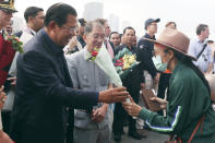 Cambodia's Prime Minister Hun Sen, left, gives a bouquet of flowers to a passenger who disembarked from the MS Westerdam, owned by Holland America Line, at the port of Sihanoukville, Cambodia, Friday, Feb. 14, 2020. Hundreds of cruise ship passengers long stranded at sea by virus fears cheered as they finally disembarked Friday and were welcomed to Cambodia. (AP Photo/Heng Sinith)