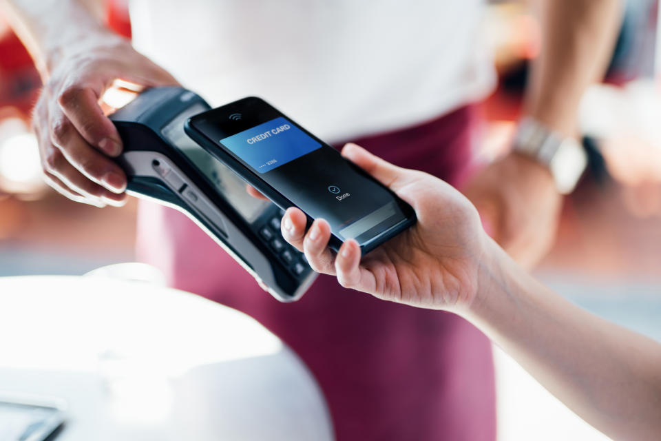 Close-up shot of a female hand using her smart phone to scan and pay for a bill at the restaurant during the day. Contactless payment, Technology Concept.