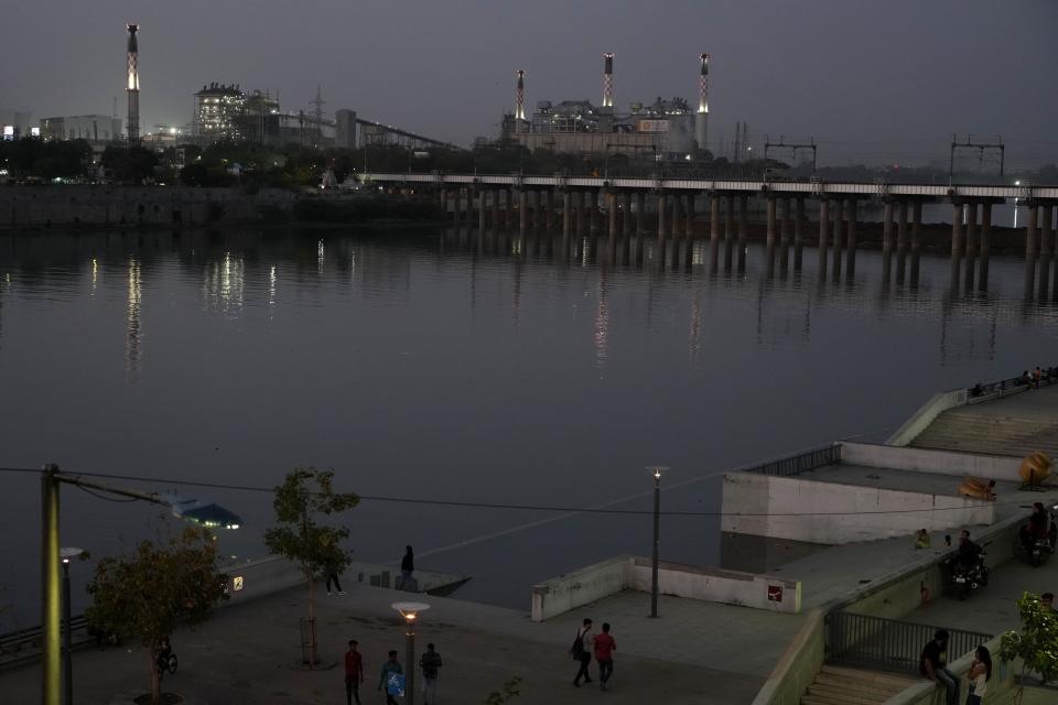 People walk with the background of the Sabarmati River and the coal-based AMGEN power plant of Torrent Power in Ahmedabad, India, Monday, March 27, 2023. India’s government has ordered coal-fired power plants to run at full power to avoid a repeat of last summer, when the grid was overwhelmed by demand and several northern states including West Bengal, Rajasthan and Gujarat faced regular power outages amid sweltering temperatures. (AP Photo/Ajit Solanki)