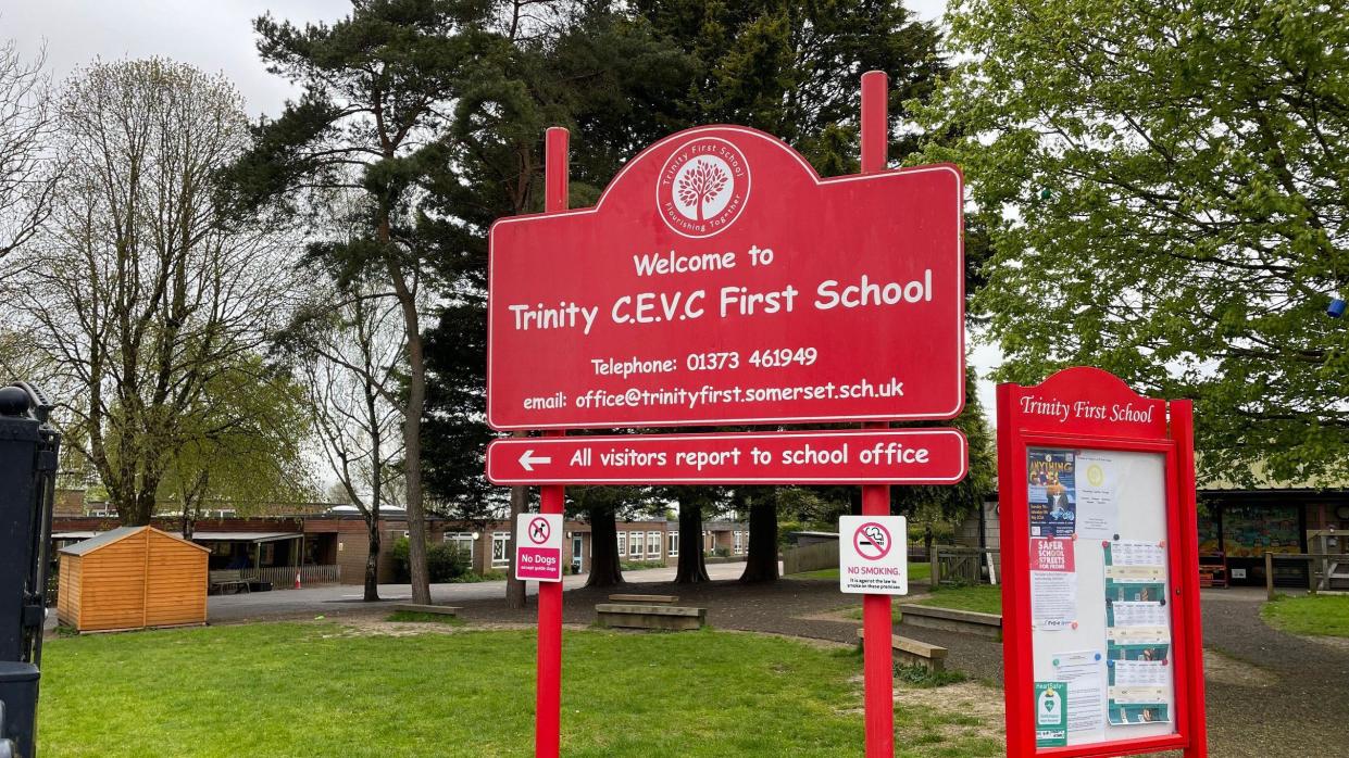 Red sign of Trinity First School with school building in background