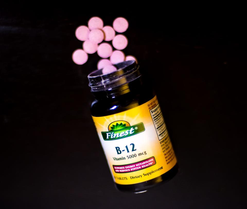 A vitamin B12 supplement container spilling pink tablets onto a black surface. 