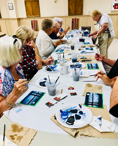 Older adults at a long table working on art projects.