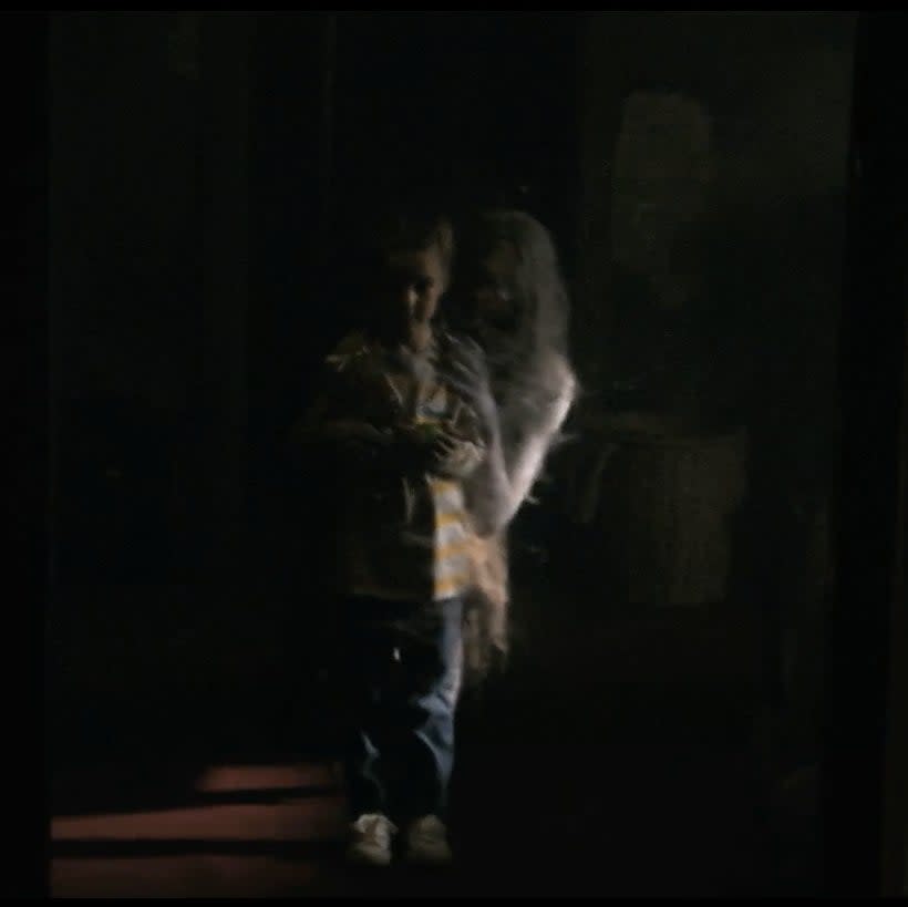 A little girl and a ghostly woman holding her in a dark room
