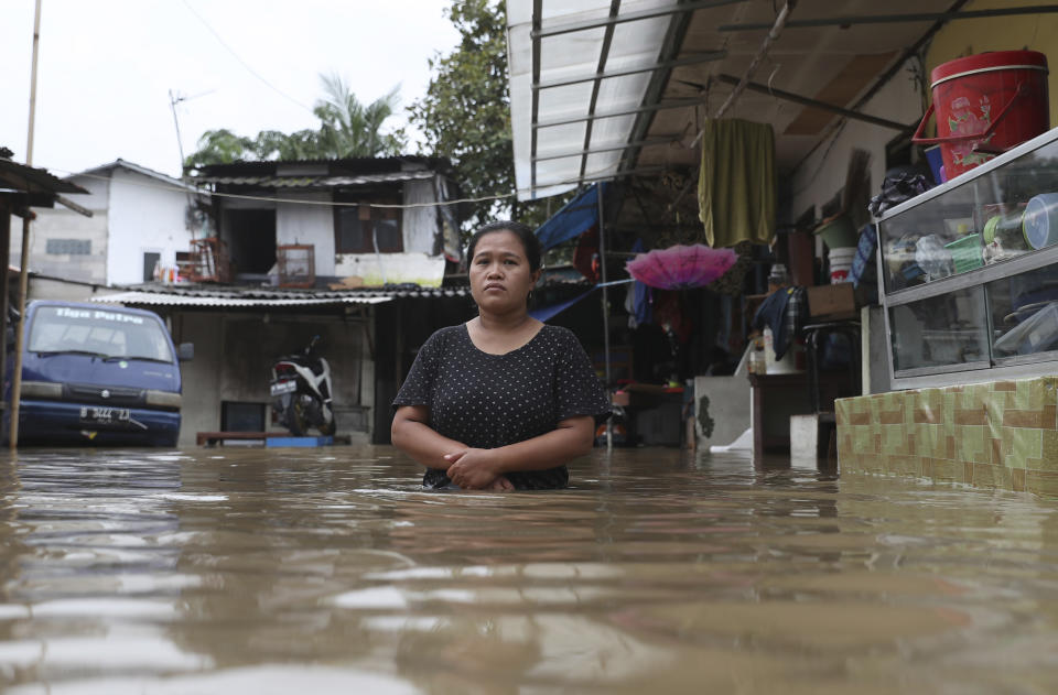 A woman pauses as she stands in flood water at a flooded neighborhood in Jakarta, Indonesia, Tuesday, Feb. 25, 2020. Overnight rains caused rivers to burst their banks in greater Jakarta sending muddy water into residential and commercial areas, inundating thousands of homes and paralyzing parts of the city's transport networks, officials said. (AP Photo/Achmad Ibrahim)