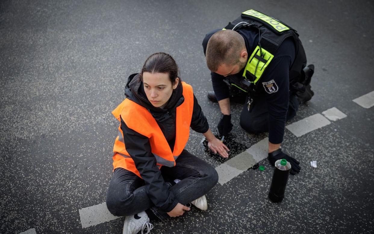 Ein Polizist löst die angeklebte Hand einer Aktivistin bei einer Straßenblockade der "Letzten Generation" in Berlin. Aus Politik und Gesellschaft wird die Forderung nach härteren Strafen laut. (Bild: SWR / Gordon Welters)