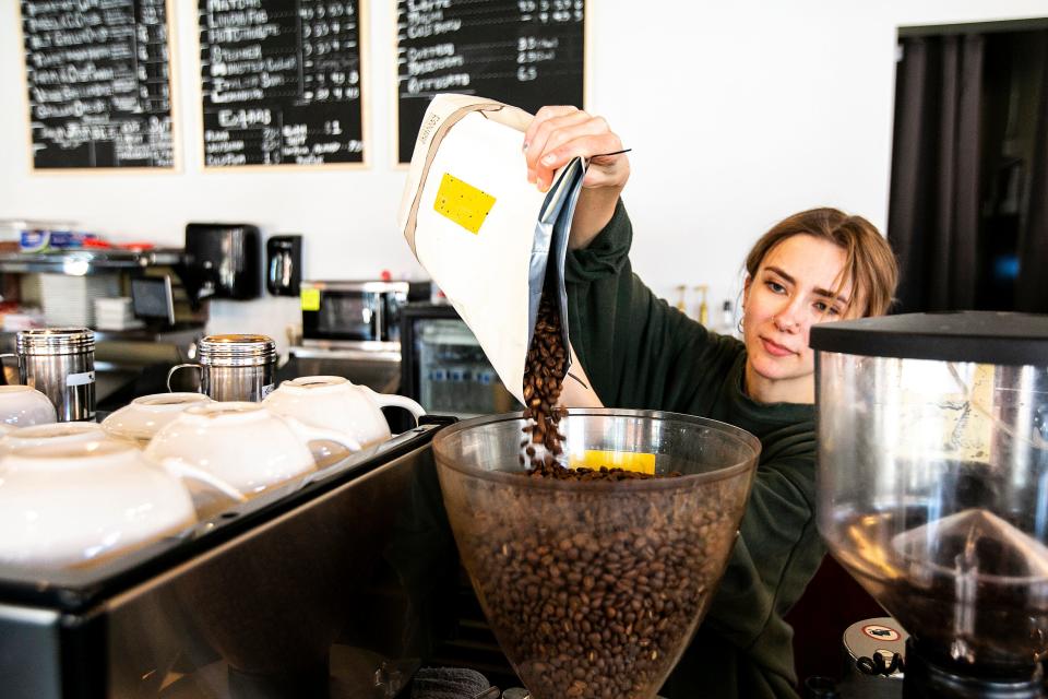 Aaliyah Warland, lead barista at Coffee Emporium, pours coffee beans into a machine, Friday, April 7, 2023, 301 E Market Street in Iowa City, Iowa.