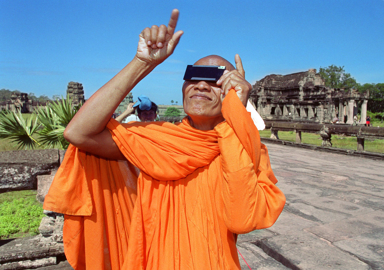 1995: A Cambodian monk, wearing safety glasses, watches the beginning of a full solar eclipse. 