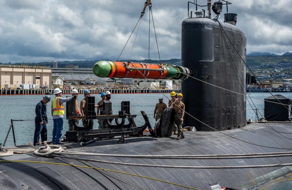 Navy sailors load a torpedo on a submarine