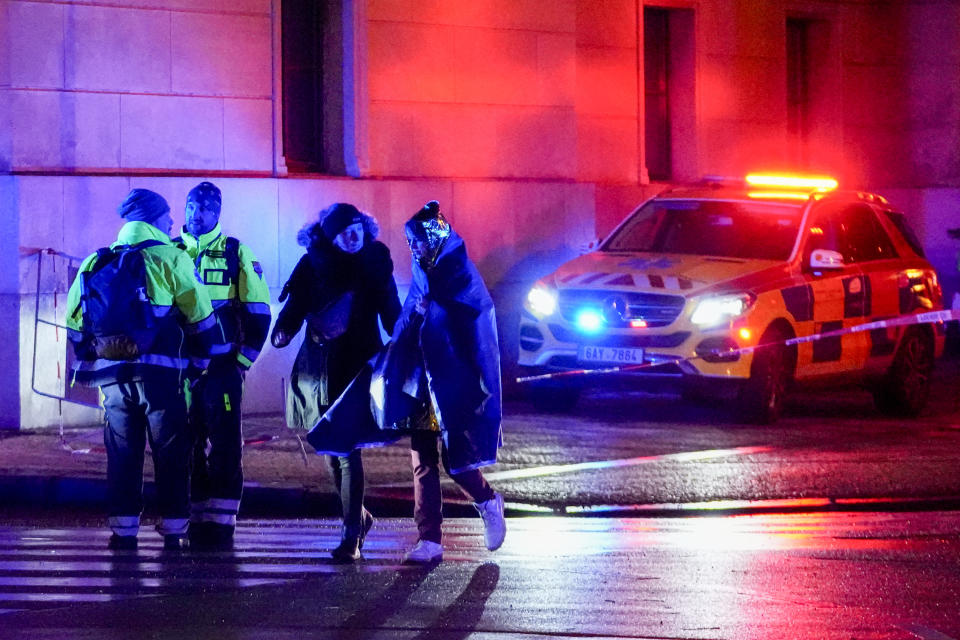 People, one wrapped in a thermal blanket, walk near the building of Philosophical Faculty of Charles University in downtown Prague, Czech Republic, Thursday, Dec. 21, 2023. A mass shooting in downtown Prague killed several people and injured others, and the person who opened fire also is dead, Czech police and the city's rescue service said Thursday. (AP Photo/Petr David Josek)
