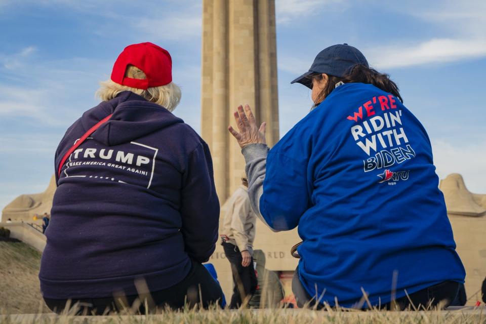 Two women conversing with their backs to the camera, one wearing a Trump shirt and the other a Biden shirt.