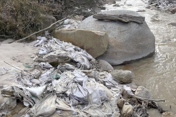 In this early 2022 image from video provided by Global Witness, a creek in Myanmar's Kachin State is lined with trash, pipes and other construction materials from a former rare earth mining site. Local villagers have said water from the creek is no longer usable for drinking or growing crops and that their skin itches after being exposed to water near rare earth mining sites. (Global Witness via AP)