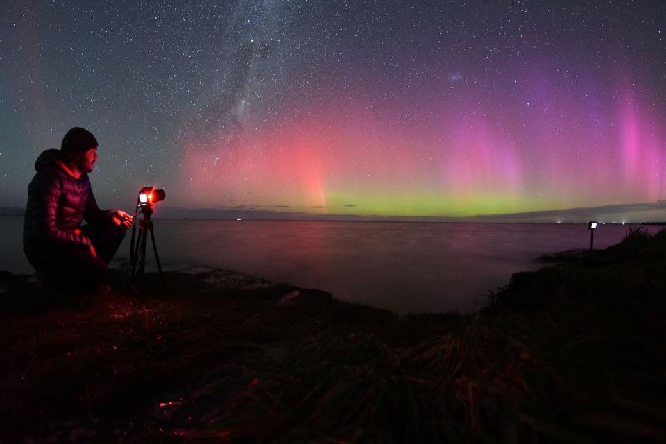 A man in heavy clothes takes pictures of the southern lights.