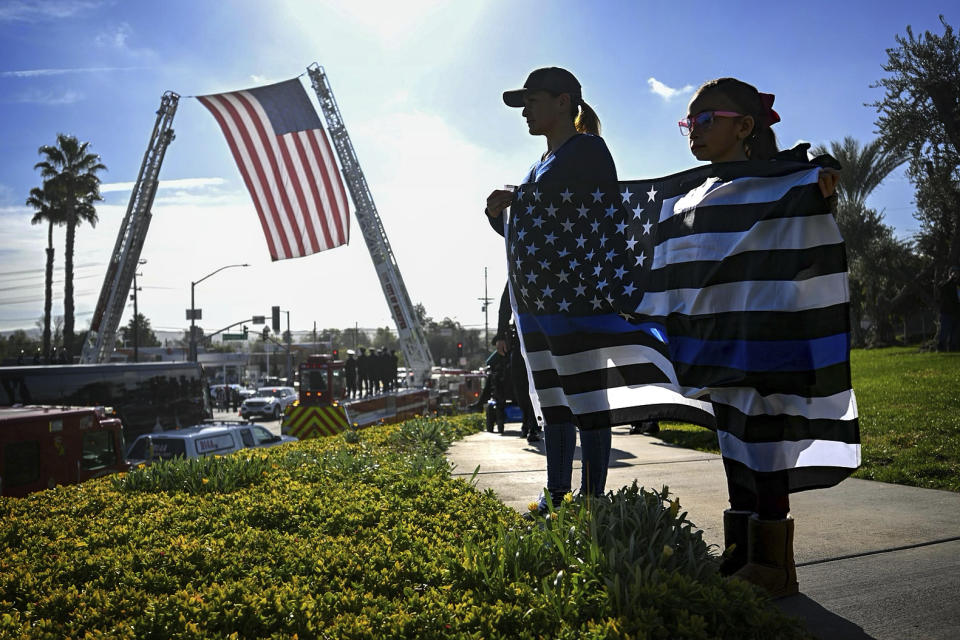 Cynthia Salazar, and daughter, Rosalynn Salazar, 7, of Corona, stand along the route to honor slain Riverside County Sheriff Deputy Isaiah Cordero as the hearse carrying his body passes by on Friday, Jan. 6, 2023, in Riverside, Calif. Cordero was shot and killed on Dec. 29, 2022, by a man with a violent criminal history during a traffic stop and the suspect later died in a shootout on a freeway, authorities said. (Watchara Phomicinda/The Orange County Register via AP)