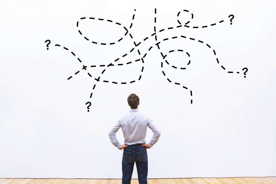 A man looks at a wall on which have been drawn question marks and dotted lines.