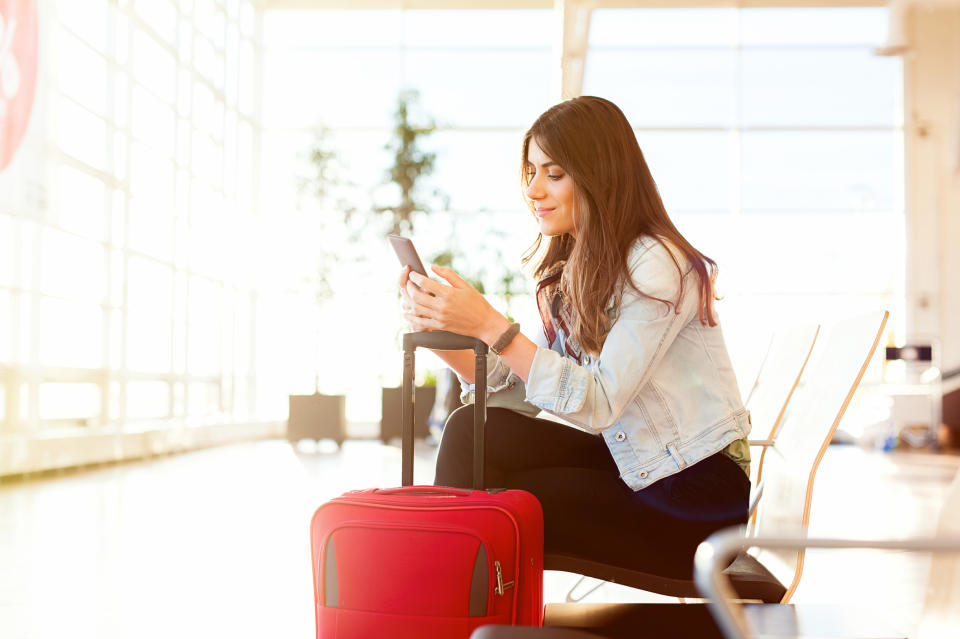 Smiling woman with suitcase typing on phone in airport