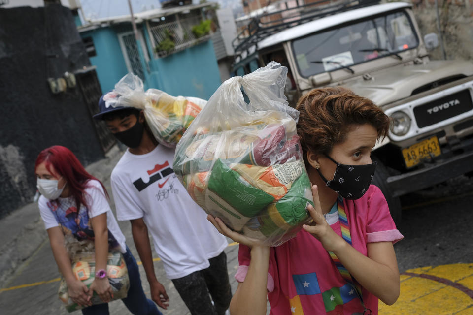 Youth carry bags of basic food staples, such as pasta, sugar, flour and kitchen oil, provided by a government food assistance program, to delivery it in the Santa Rosalia neighborhood of Caracas, Venezuela, Saturday, April 10, 2021. The program known as Local Committees of Supply and Production, CLAP, provides subsidized food for vulnerable families, especially now in the midst of a quarantine to stop the COVID-19 pandemic that has left many without income. (AP Photo/Matias Delacroix)