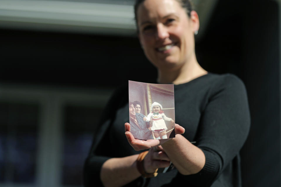 In this Wednesday, April 8, 2020, photo, Kelly Adsero poses as she holds a family photo of her as a small child with her grandfather Bill Chambers and her grandmother Barbara Jean Chambers, in Woodinville, Wash. Bill Chambers, 97, died March 14, 2020, at an adult family home where he lived with four other World War II veterans. He wasn't obviously ill, but tested positive for the new coronavirus after he died. (AP Photo/Ted S. Warren)