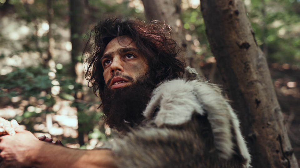 Close-up Portrait of Primeval Caveman Wearing Animal Skin and Fur Hunting with a Stone Tipped Spear in the Prehistoric Forest. Prehistoric Neanderthal Hunter Ready to Throw Spear in the Jungle