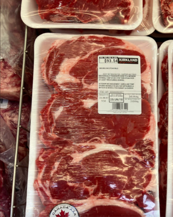 A package of Kirkland ribeye steaks is priced at $93.54, featuring three large cuts of meat in plastic wrap.  Canadian AAA grade, weight and barcode visible