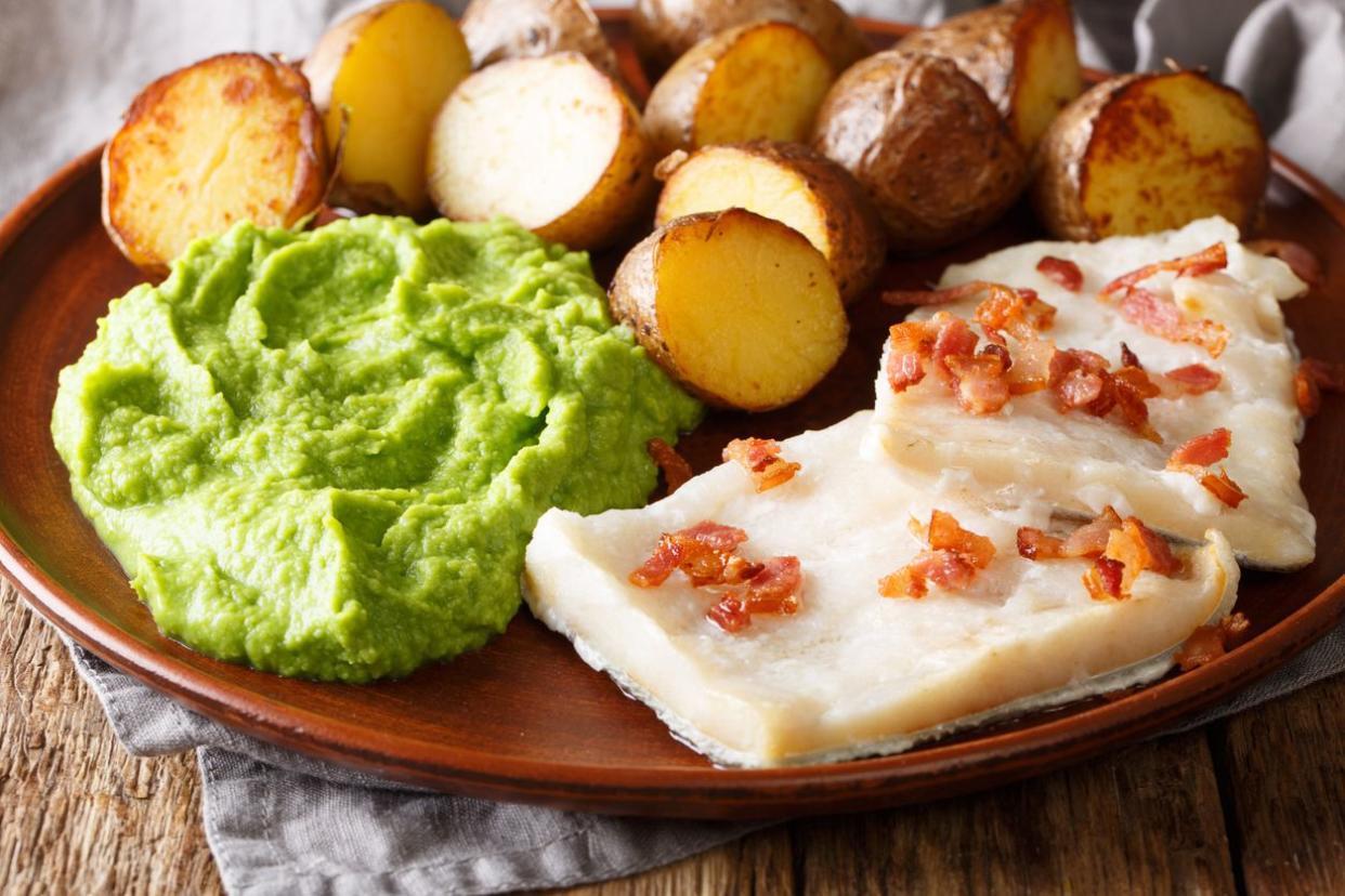 Popular Scandinavian food Lutefisk cod with pea puree, baked potatoes and bacon close-up on a plate on the table