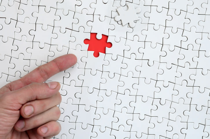 A finger pointing to a missing puzzle piece in a large puzzle.