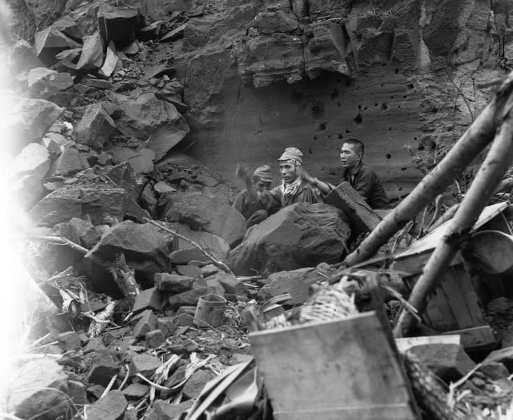 Three Japanese soldiers emerge from their hiding place to surrender during mopping up operations