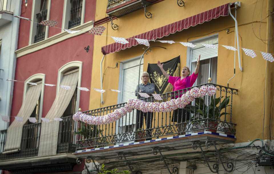 In this photo taken on Saturday April 25, 2020, a woman sings on her decorated balcony during the annual traditional April Fair in Seville, Spain. Without breaking the confinement rules and maintaining their distance from each other, the residents from their balconies, celebrated the tradition of the fair which has been cancelled due to the coronavirus outbreak and normally includes flamenco dancing, bullfighting, eating and drinking. (AP Photo Miguel Morenatti)