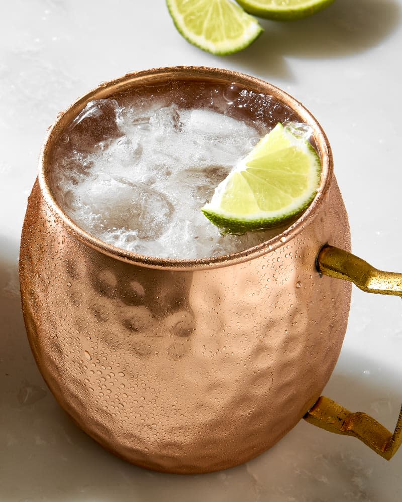 overhead shot of a moscow mule being poured into a copper mug, with a lime to the left of the mug.