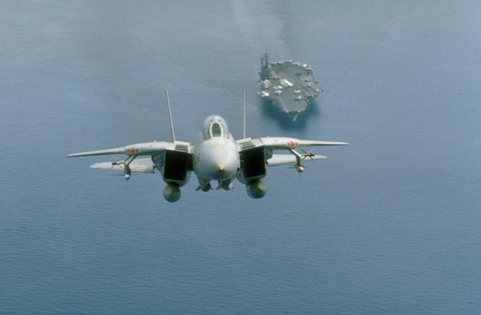 An F-14A Tomcat aircraft takes off from the aircraft carrier USS America (CV-66), seen in the distance