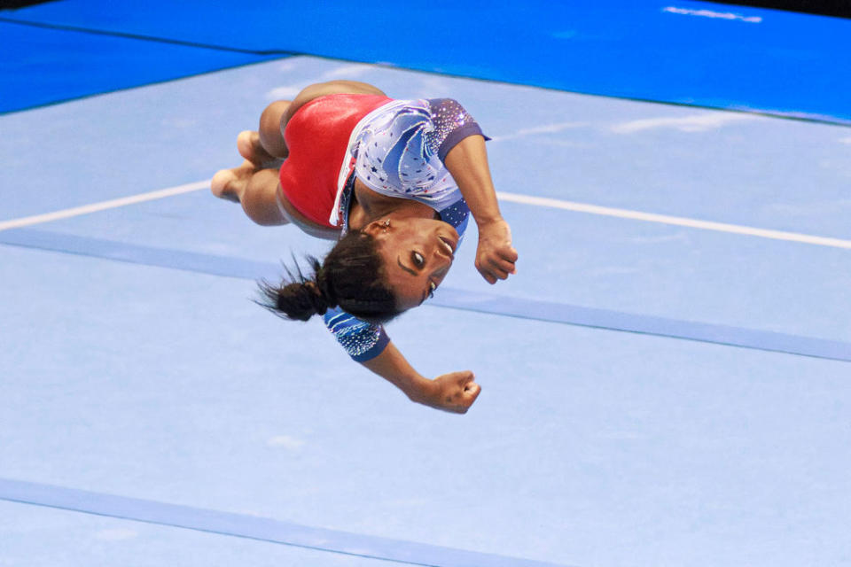 Simone Biles performing a mid-air flip in a gymnastics event, wearing a leotard