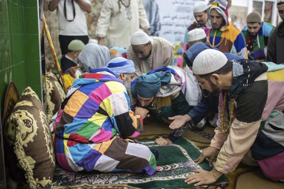 Members of the Sufi Karkariya order reach out to kiss the hands of their leader during a religious celebration of the prophet Muhammed's birthday, in Aroui, near Nador, eastern Morocco, Monday, Oct. 18, 2021. It was the first such gathering since the pandemic. The order, the Karkariya, follows a mystical form of Islam recognizable by its unique dress code: A modest yet colorful patchwork robe. (AP Photo/Mosa'ab Elshamy)