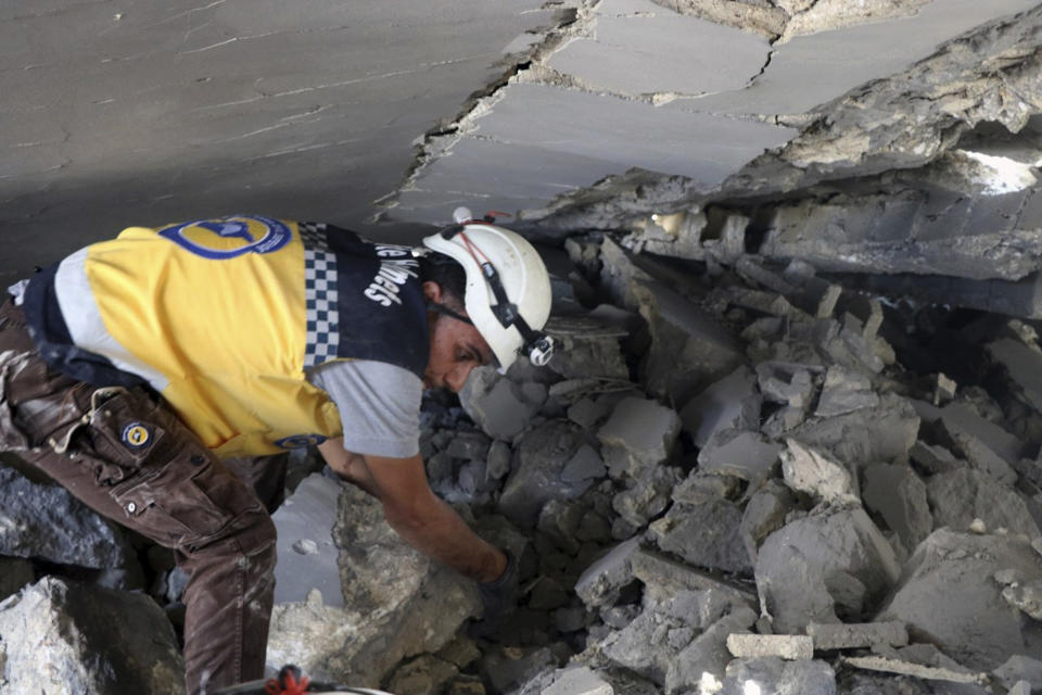 This photo posted and provided by the Syrian Civil Defense White Helmets, which has been authenticated based on its contents and other AP reporting, shows a Civil Defense worker searching for victims under the rubble after an airstrike by Syrian government forces hit the town of Maaret al-Numan in Idlib province, Syria, Saturday, June. 15, 2019. Syrian opposition activists say government airstrikes on rebel-held areas in northwestern Syrian and intense fighting claimed the lives dozens of people. (Syrian Civil Defense White Helmets via AP)