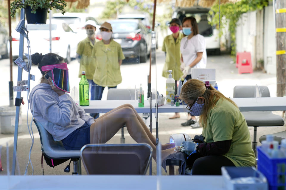 FILE - In this July 22, 2020, file photo, Tyson Salomon, left, gets a pedicure outside Pampered Hands nail salon in Los Angeles California's top health official says the state will no longer require social distancing and will allow full capacity for businesses when the state reopens on June 15, 2021. State health director Dr. Mark Ghaly said Friday, May 21, that the state envisions loosening many of its rules in mid-June as coronavirus cases continue to fall and vaccine rates continue to rise. (AP Photo/Ashley Landis, File)