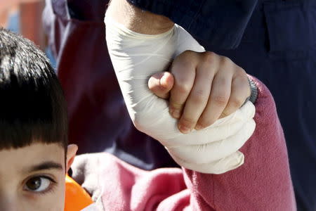 A toddler holds the hand of a Greek Coast Guard officer, after being retrieved from a dinghy carrying refugees and migrants aboard the Ayios Efstratios Coast Guard vessel, during a rescue operation in the open sea between the Turkish coast and the Greek island of Lesbos, February 8, 2016. REUTERS/Giorgos Moutafis