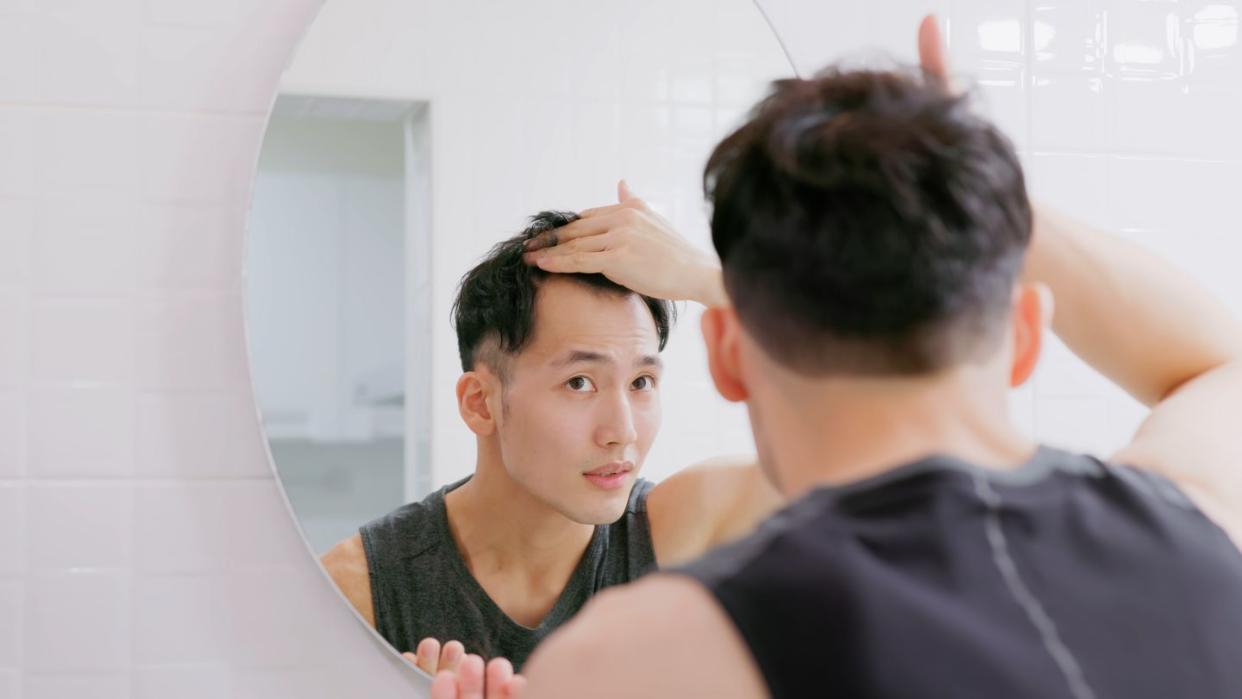 young handsome asian man in front of the mirror checking his hairline