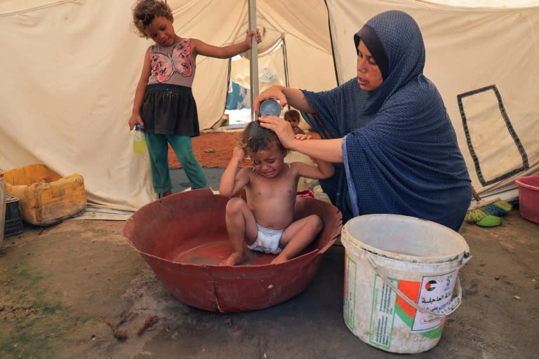 Una madre baña a su hijo en una tienda de un campamento de desplazados en Deir el Balah, en el centro de la Franja de Gaza, el 8 de julio de 2024 (Eyad Baba)