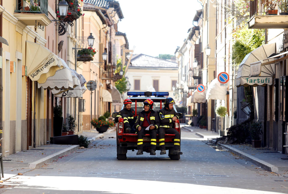 Firefighters are seen on the back of car as they inspect in the ancient city of Norcia following an earthquake in central Italy
