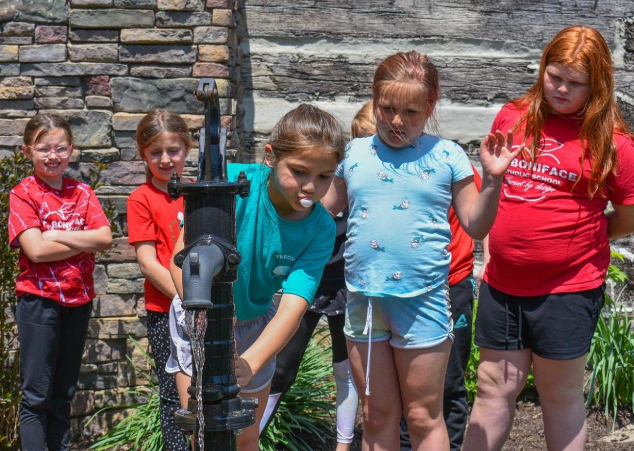 Students from R.C. Waters Elementary School and St. Boniface Catholic School take turns pumping water from a well on the grounds of the Oak Harbor Log Cabin.