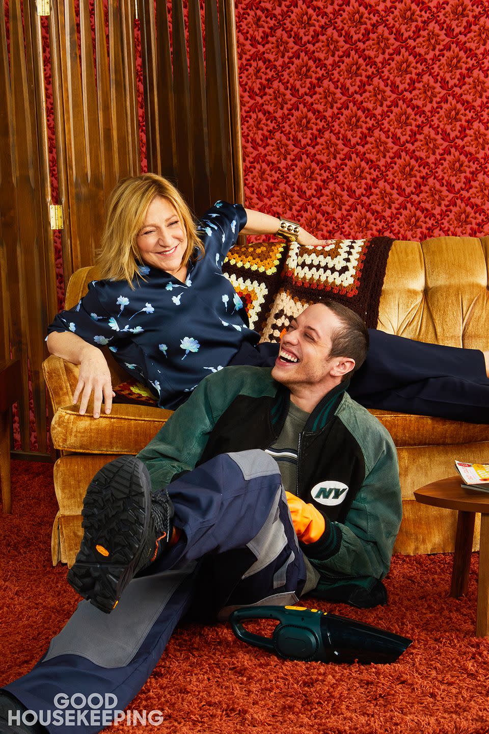 pete davidson sitting on shag rug laughing with edie falco sitting on a couch