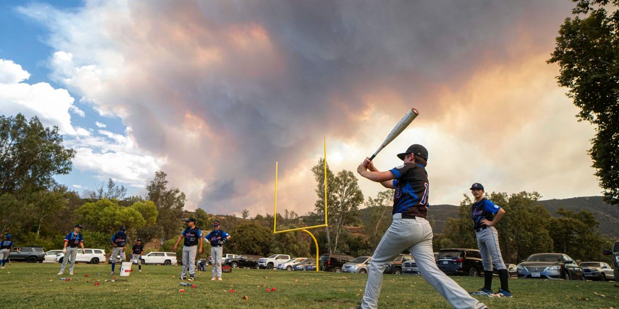 TOPSHOT - Little League players warm-up before a game as a brush fire is ablaze in back at a field next to the Sycuan Casino on the Sycuan Indian reservation during the Valley Fire, near Dehesa, in San Diego, California on September 6, 2020. - The Valley Fire in the Japatul Valley burned 4,000 acres overnight with no containment and 10 structures destroyed, Cal Fire San Diego said. (Photo by SANDY HUFFAKER / AFP) (Photo by SANDY HUFFAKER/AFP via Getty Images)