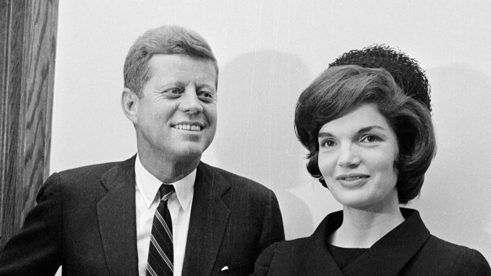 John Fitzgerald Kennedy, Jr., is photographed for the first time at the age of 13 days during his christening in the Georgetown University Hospital Chapel here, December 8th. The infant is being held by his mother, Mrs. Jacqueline Kennedy. The proud papa, President-elect John F. Kennedy, smiles beside her.